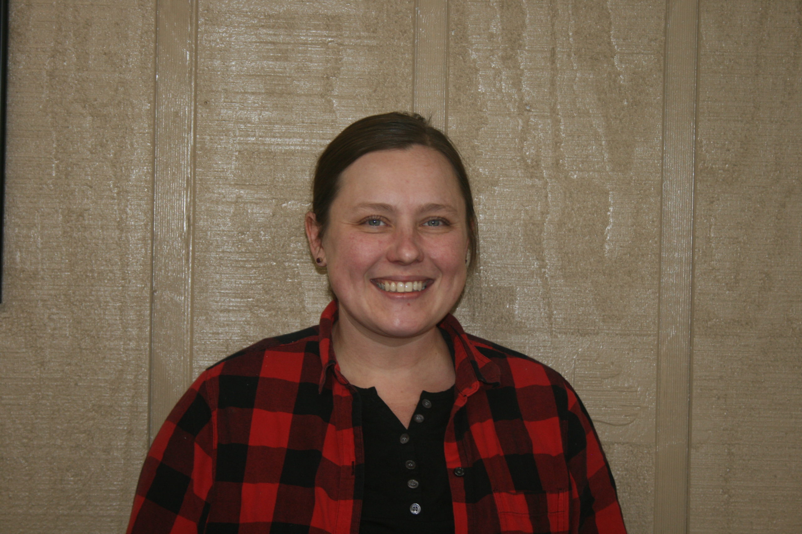 A woman in a red and black plaid shirt smiling